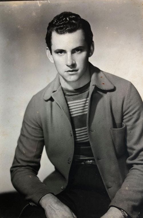 Black and white portrait of a young man sitting with a serious expression, wearing a striped shirt and a cardigan.